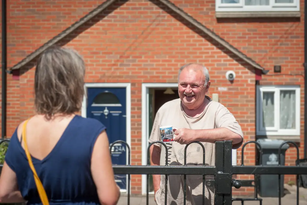A GSA customer smiling while holding a mug and chatting with a housing officer near his home.
