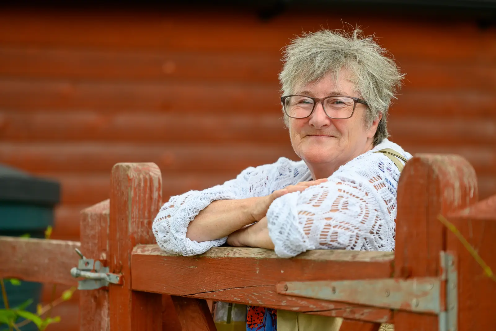A smiling lady learning on a gate