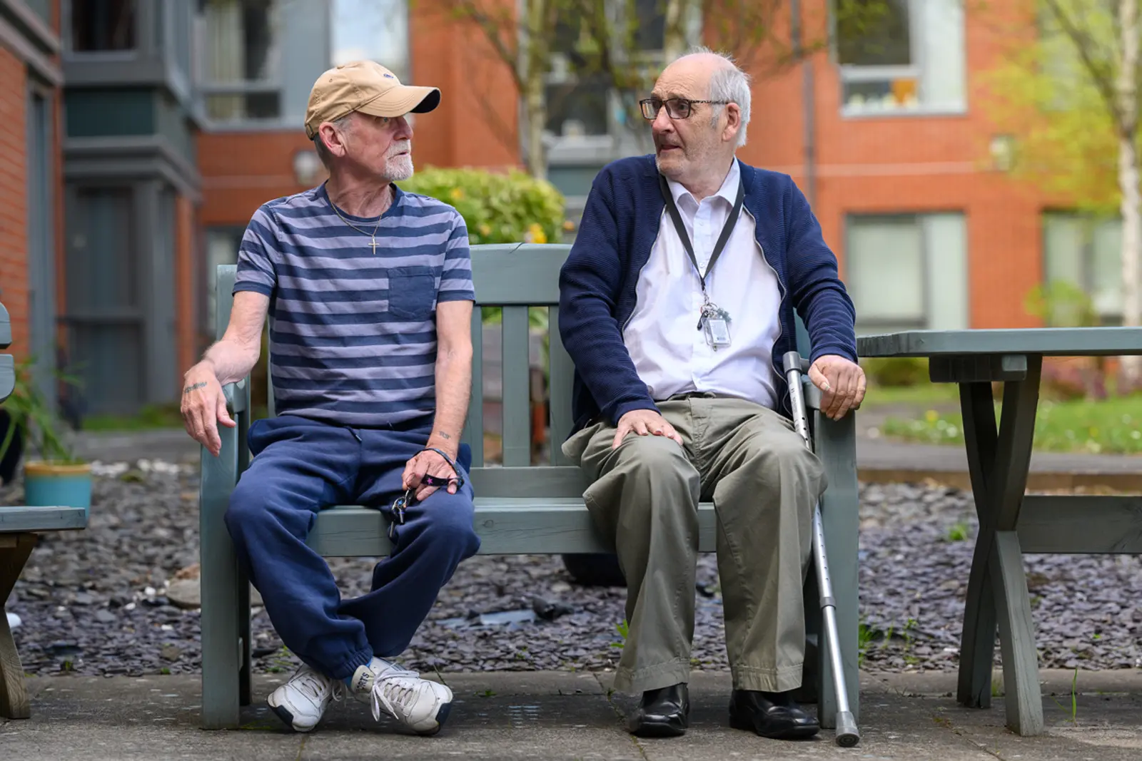 Two men talking on a bench outside a residential building