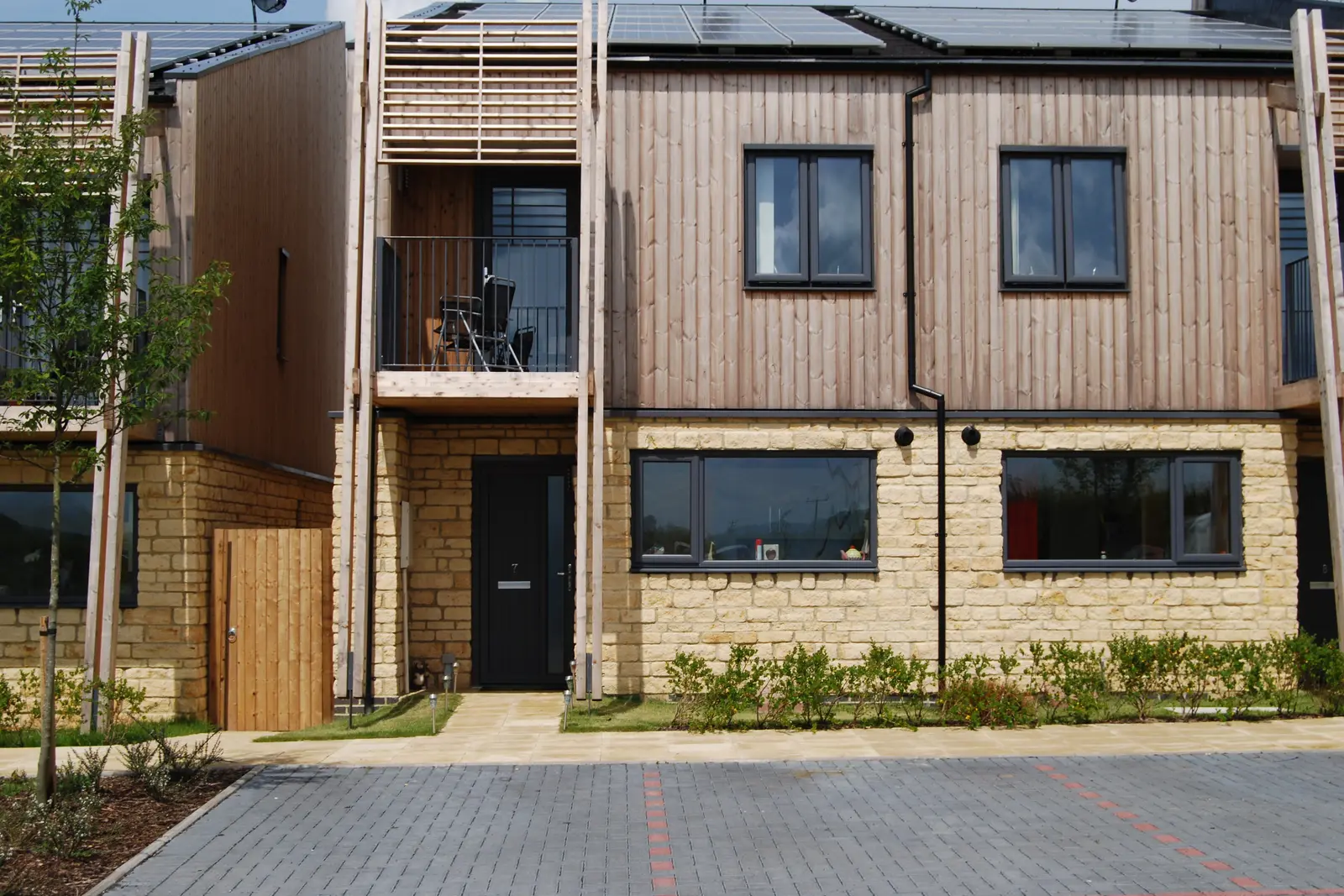 A semi-detached brick and wood fronted home with a first-floor balcony
