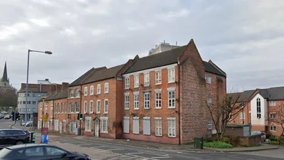 Three-storey red brick apartment building located on a street corner, with several parked cars opposite.