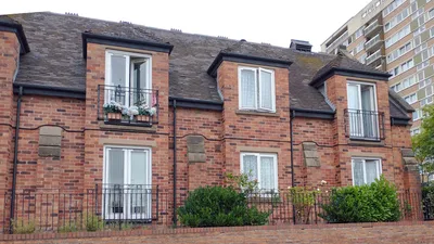 A brick residential building named Tantarra Court, featuring multiple windows and small balconies. The structure has a sloped roof and is enclosed by a metal fence, with greenery visible in the foreground.