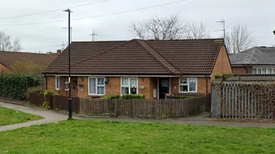 A brick bungalow on Edison Road with a dark brown tiled hipped roof, white‑framed windows, and a small front garden bordered by a low wooden fence. A lamppost stands on the pavement in front, with grass and a hedge lining the walkway.