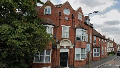 Exterior view of a large red brick building on Park Lane, featuring three storeys with a distinctive architectural style. The facade includes multiple bay windows on the ground and first floors, white-framed windows throughout, and a central entrance with a black double door topped by an ornate white stone arch.