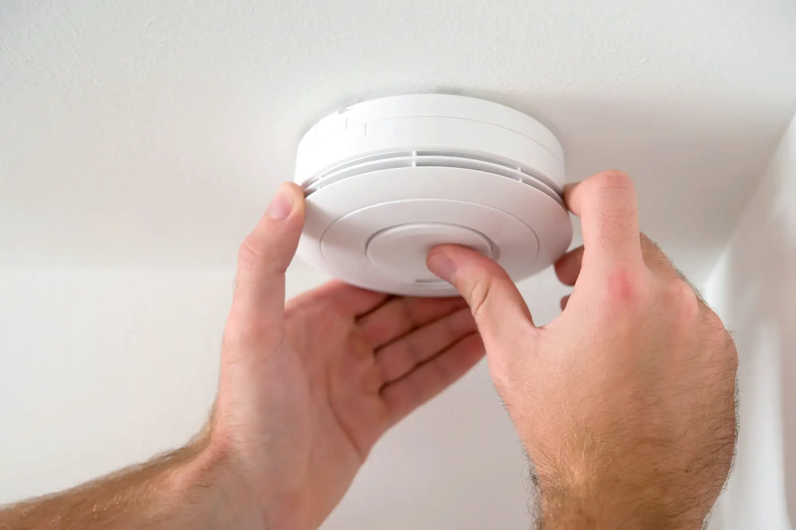 A close-up shot of two hands testing a smoke alarm
